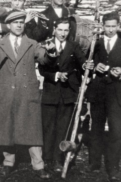 Musician holding a basic charrasco, a requinta traverse flutist and bass drummer standing behind, ca. 1920